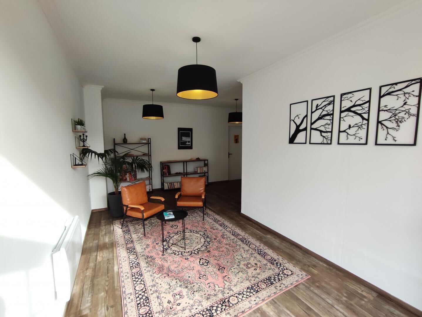 Un salón con dos sillones de cuero, un tapete estampado, lámparas colgantes negras y cuadros en la pared.