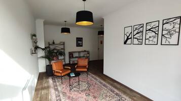 Un salón con dos sillones de cuero, un tapete estampado, lámparas colgantes negras y cuadros en la pared.