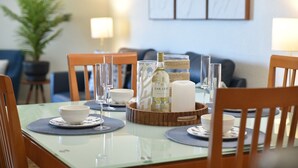 Een eetgedeelte met een glazen tafel, houten stoelen, helder glaswerk, een fles wijn en een kaars.