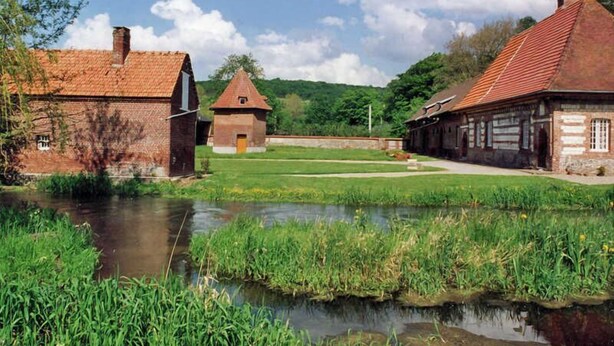 A rural setting with traditional brick buildings, a small pond, and a clear sky. - Gîtes de France® - La Masûre (ST MARTIN LE GAILLARD)