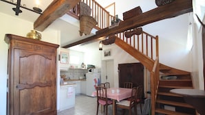 A cozy kitchen with a wooden cabinet, a dining table with chairs, and a staircase leading to an upper level. - Gîtes de France® - La Masûre (ST MARTIN LE GAILLARD)