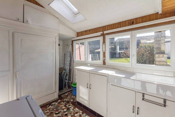 A kitchen with white cabinets, a window with a view of the garden, and a tiled floor.