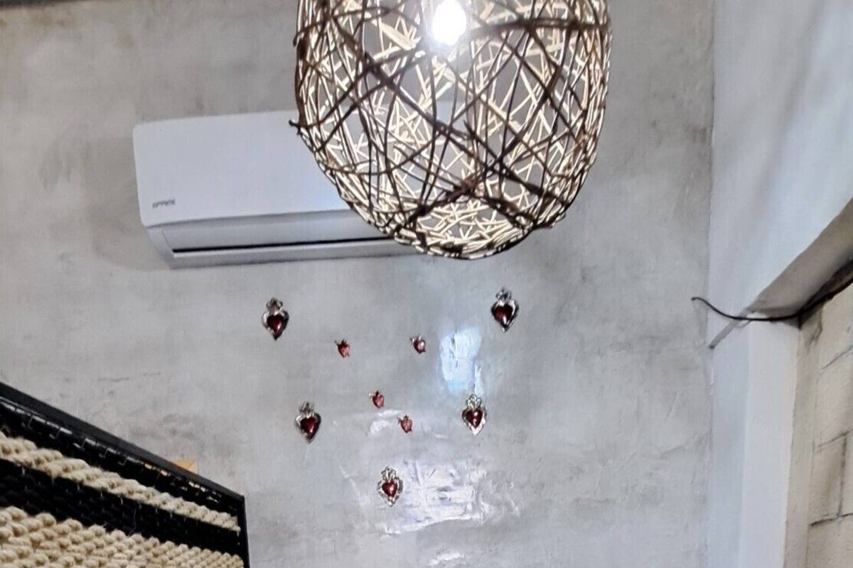 Une chambre à coucher comprenant un lit, un luminaire suspendu, un climatiseur fixé au mur et un mur à texture.