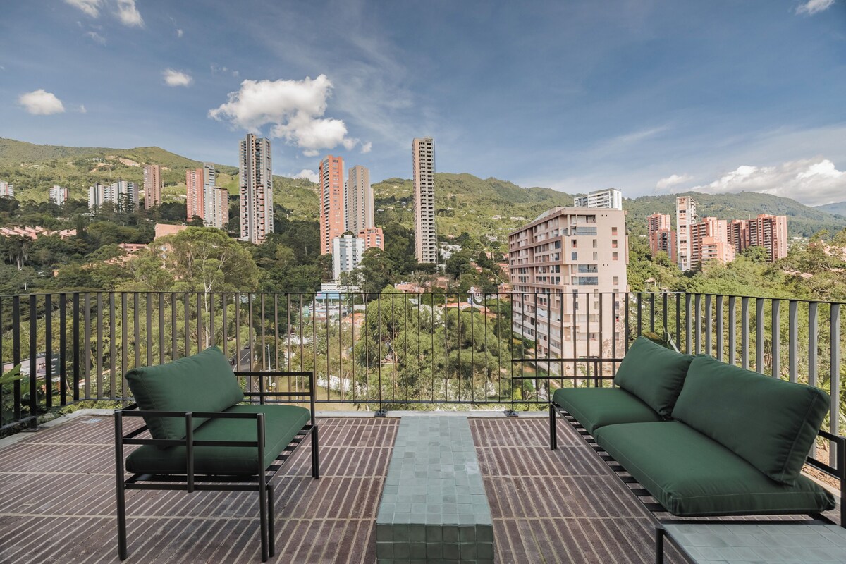 Un balcon doté de deux coins salons avec des assises rembourrées de couleur verte et d’une rambarde en métal.