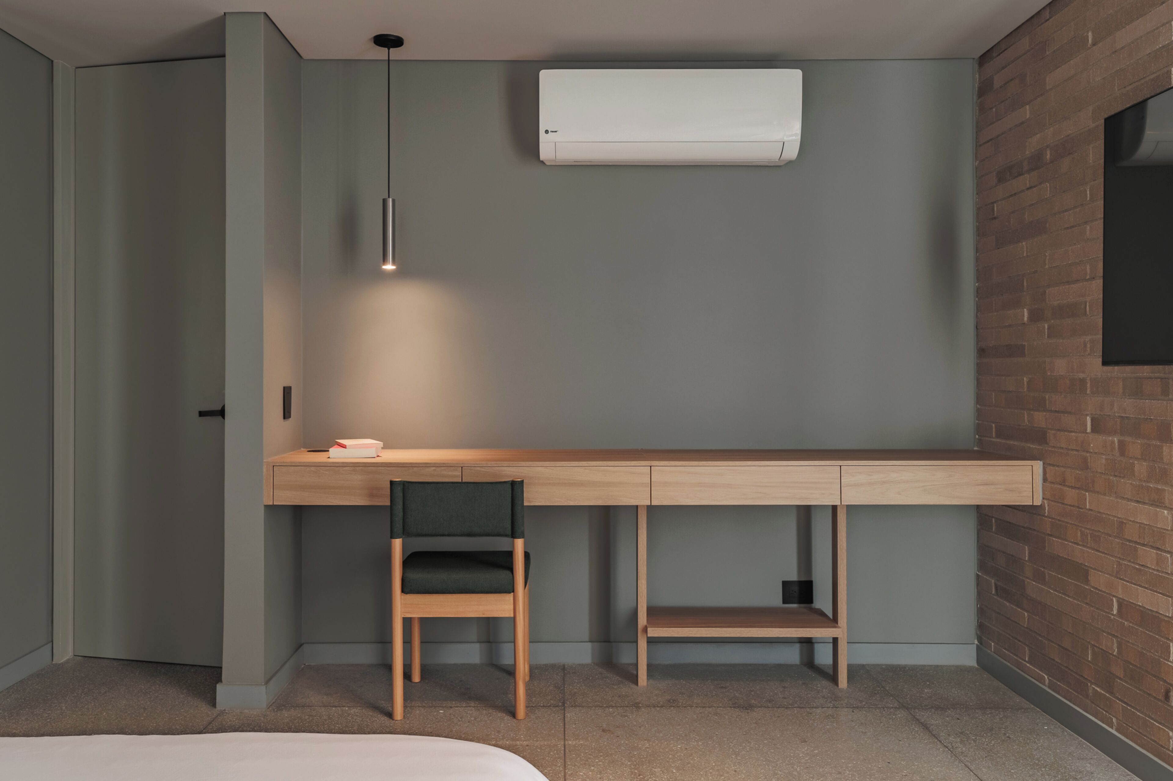 Un dormitorio moderno con escritorio empotrado, una silla, una lámpara colgante y aire acondicionado instalado.