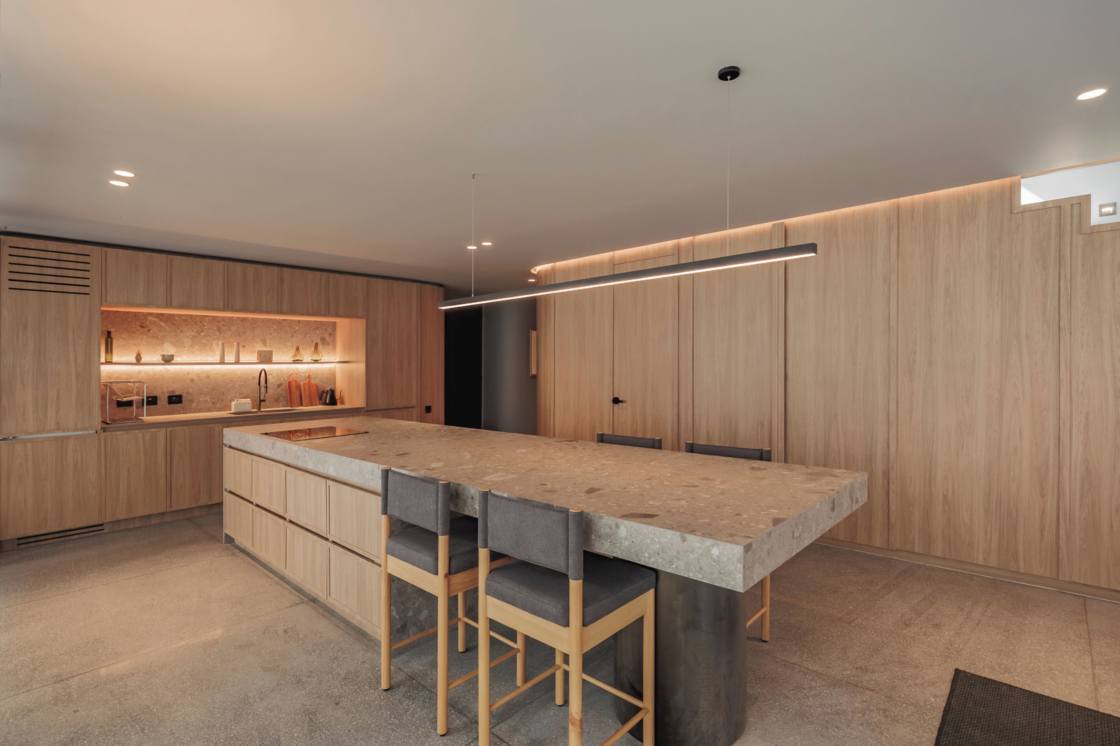 A modern kitchen with wooden cabinetry, a central island with bar stools, and built-in appliances.