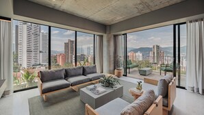 Ein geräumiges Wohnzimmer mit einer großen Couch, einem Couchtisch und Blick auf eine Stadtlandschaft durch große Fenster.