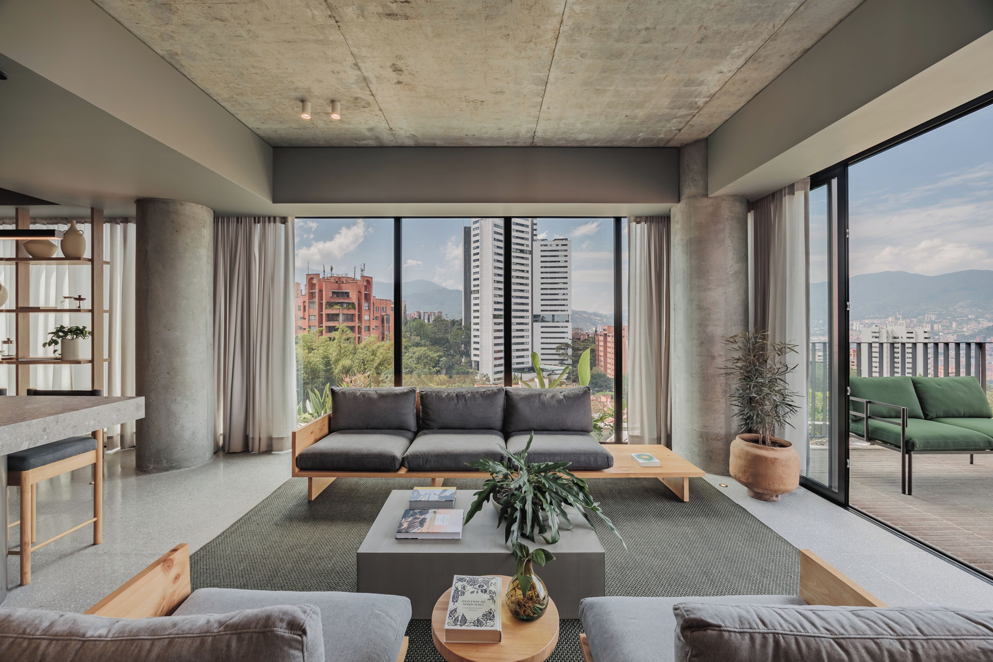A modern living room with a large sofa, a coffee table, and a view of the cityscape through large windows.