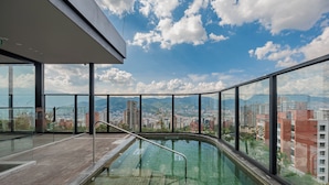 Een dakzwembad met glazen balustrade, met een panoramisch stadsgezicht.