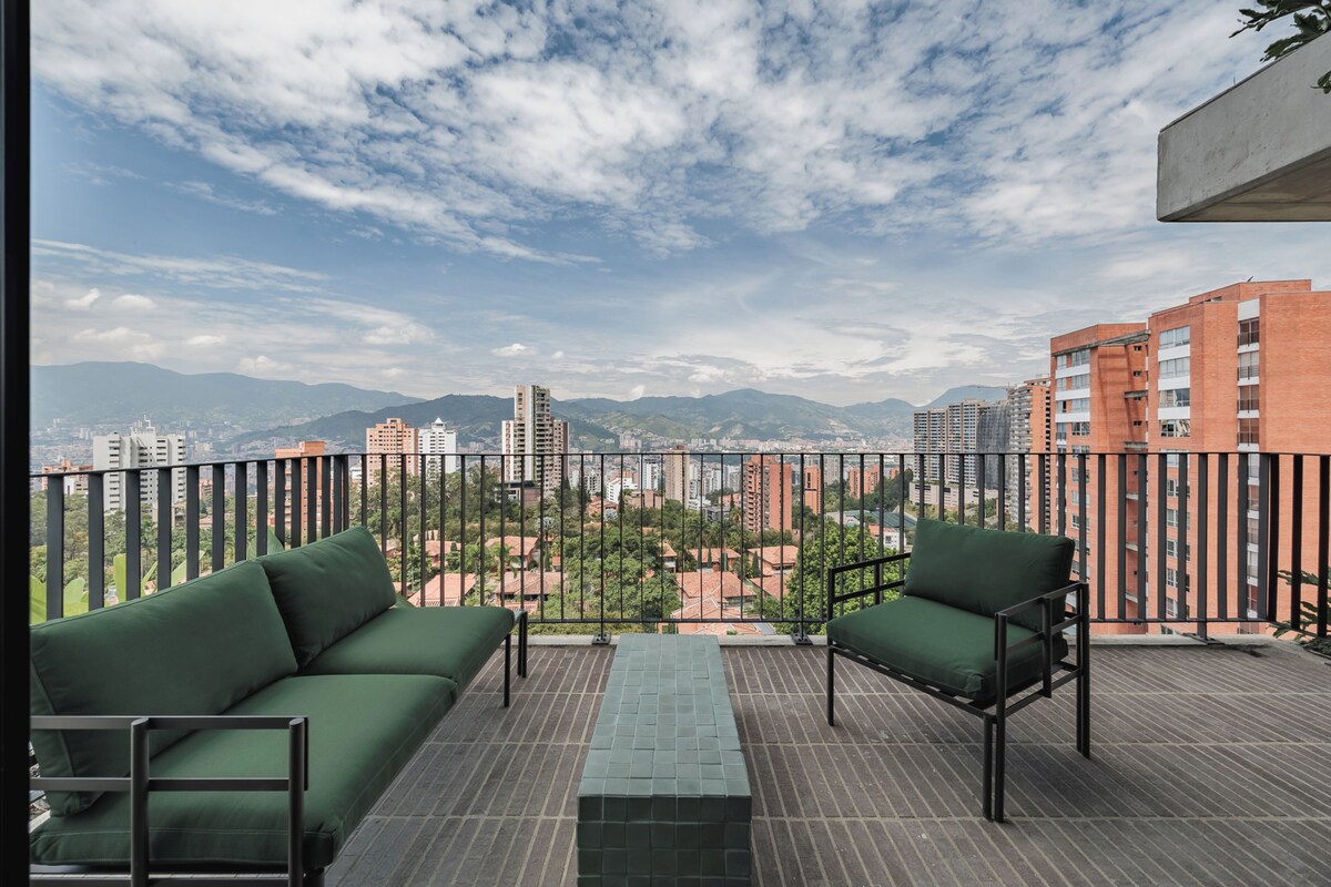Un balcon doté de mobilier vert, d’un sol carrelé et offrant une vue sur la ville.