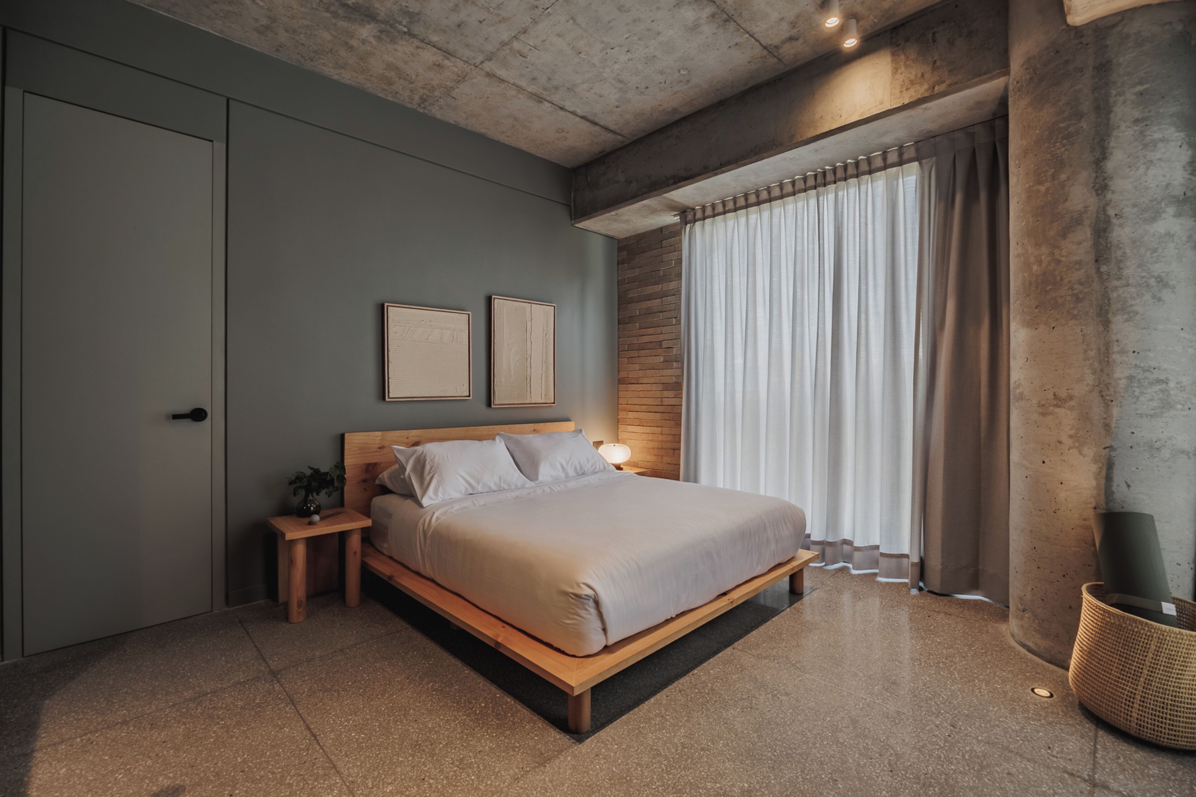 A modern bedroom with a bed, bedside tables, a nightstand, a potted plant, and a large window with curtains.