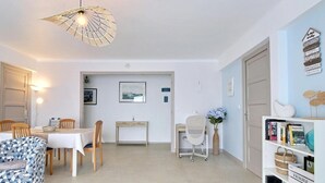 Un coin repas avec une table, des chaises et un luminaire suspendu. On y trouve également un bureau avec une chaise et un vase rempli de fleurs.