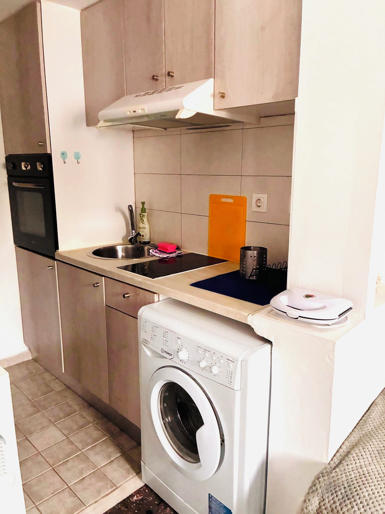 A compact kitchen with a built-in oven, a sink, and a washing machine.