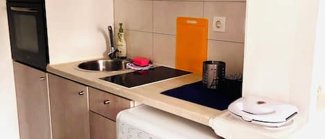 A compact kitchen with a built-in oven, a sink, and a washing machine.