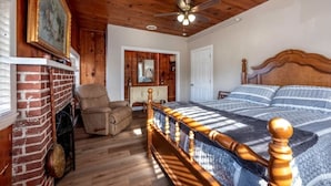 A bedroom with a wooden ceiling, a bed with a patterned bedspread, a chair, and a fireplace. - Incredible Views! Historic Branson Home, two Porch Swings (Branson)