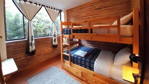 A bunk bed room with a brick wall, a window with curtains, and a small desk.