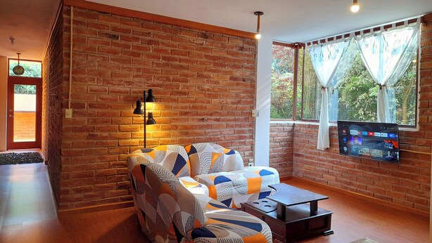 A cozy living room with a brick wall, a patterned sofa, a coffee table, and a TV mounted on the wall.