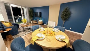 A dining area with a round table set for four, blue chairs, and a TV mounted on the wall. - Oceanfront 1 BR w/ Pool and Heated Pool (Redondo Beach)