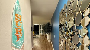A hallway with a surfboard sign, wooden flooring, and a wall decorated with multiple mirrors. - Oceanfront 1 BR w/ Pool and Heated Pool (Redondo Beach)
