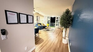 A modern living room with a blue sofa, a coffee table, and a potted plant. There are framed documents on the wall and a door leading to another room. - Oceanfront 1 BR w/ Pool and Heated Pool (Redondo Beach)