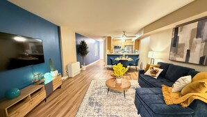 A modern living room with a blue sofa, a coffee table, and a TV on the wall. - Oceanfront 1 BR w/ Pool and Heated Pool (Redondo Beach)
