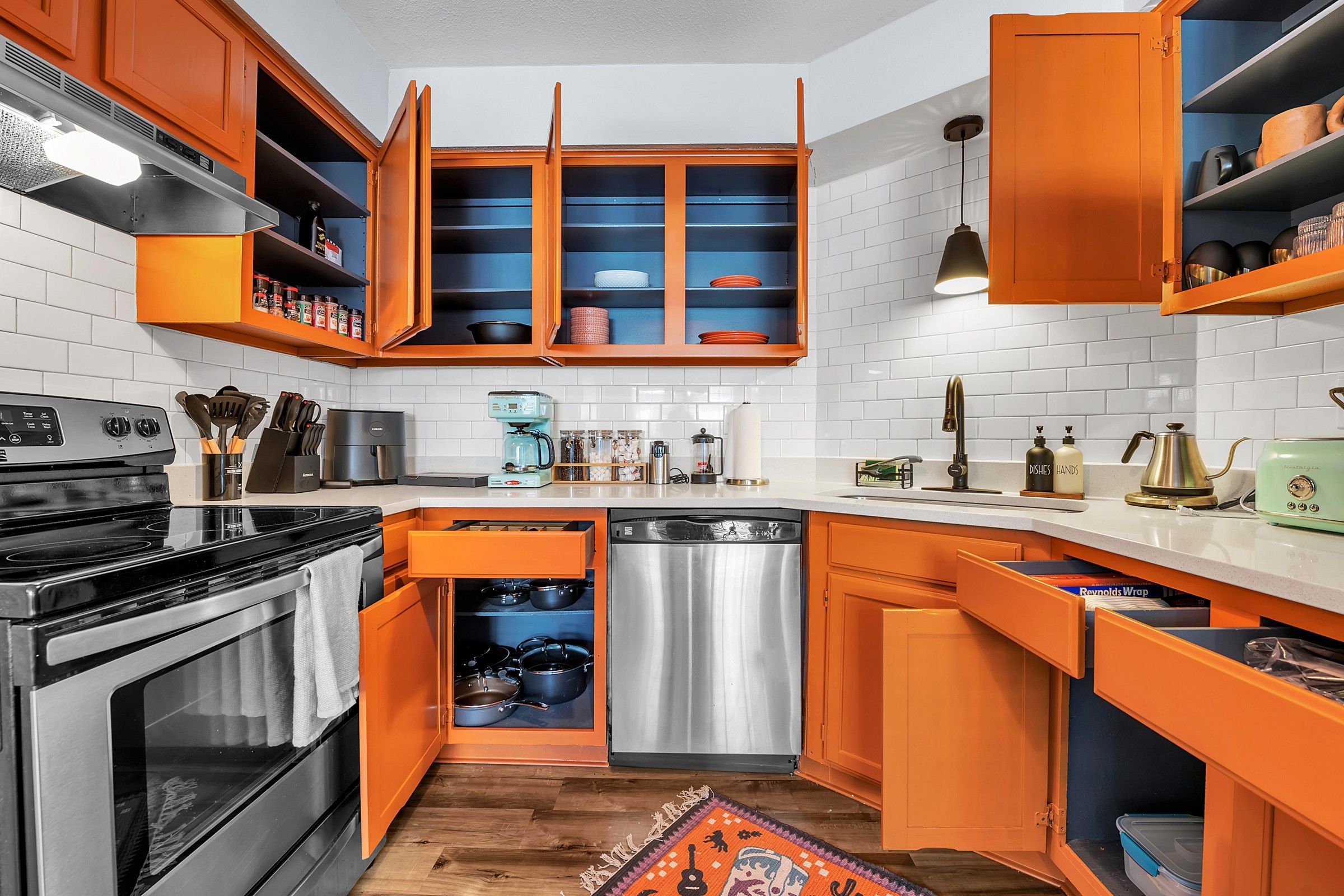 A kitchen with orange cabinets, a stainless steel dishwasher, and a black stove.