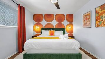 A modern bedroom with a green upholstered bed, a ceiling fan, and a wall with circular patterns.