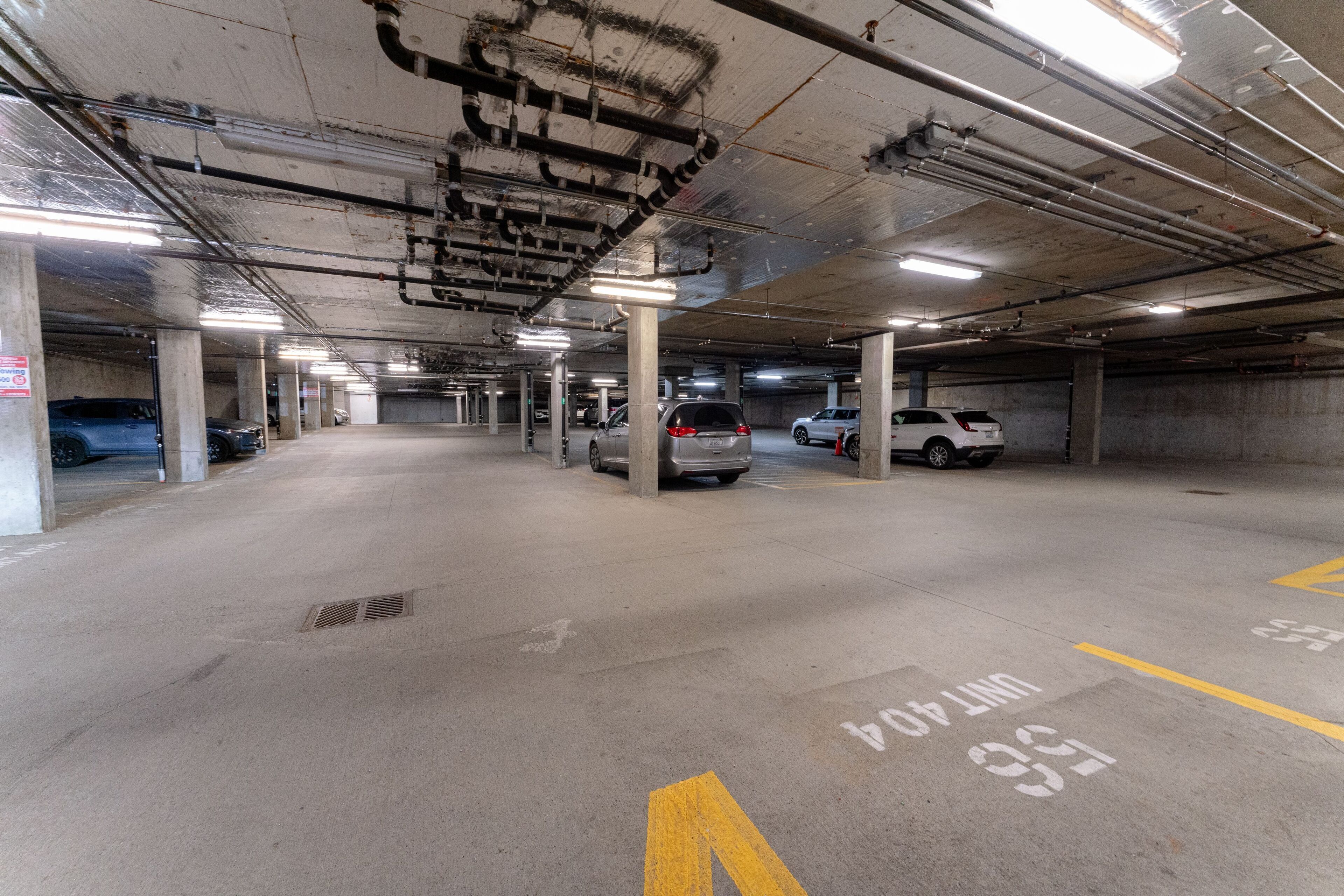 Eine Tiefgarage mit Betonpfeilern, markierten Parkplätzen und Deckenbeleuchtung.