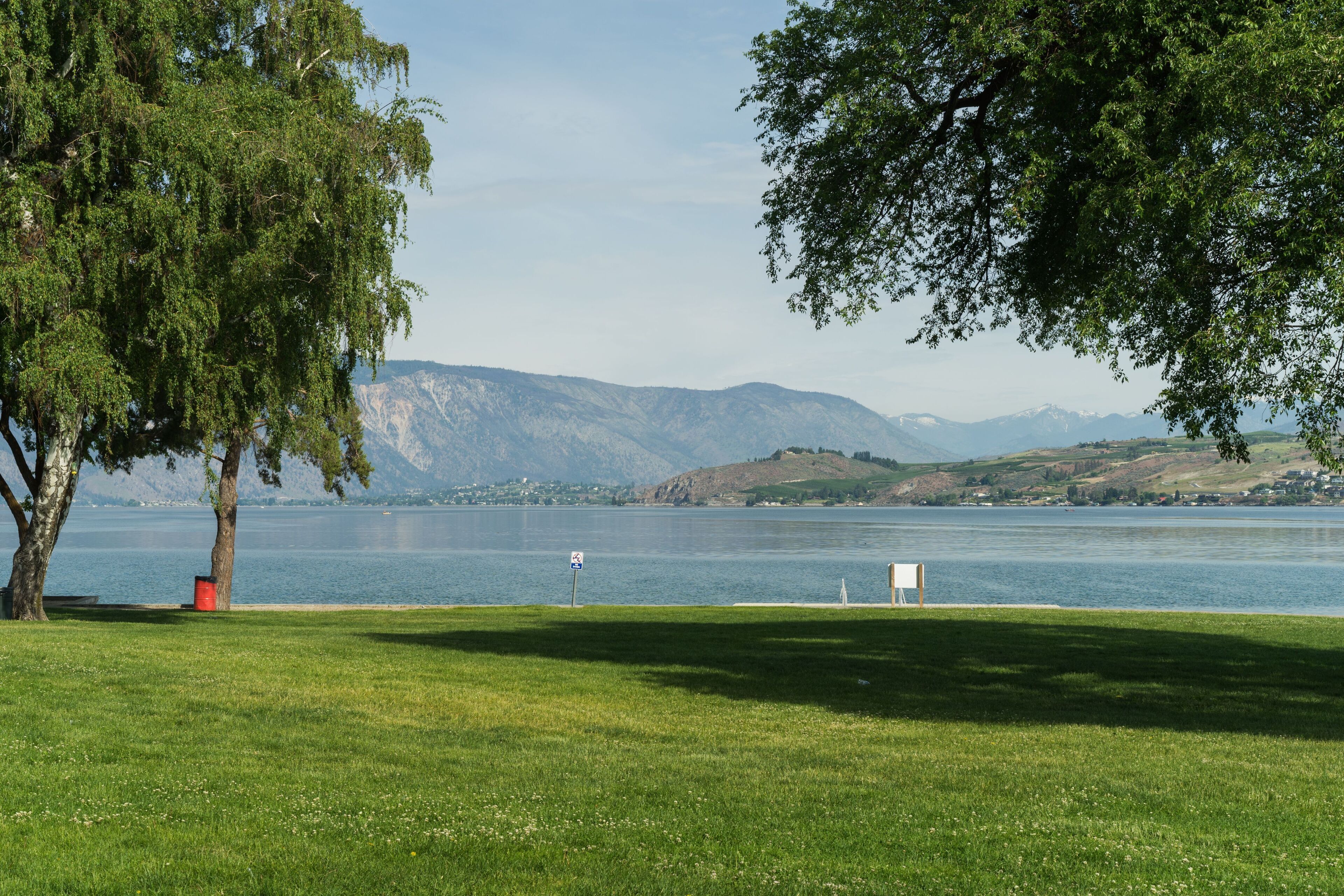 A spacious green lawn borders the lake, offering sweeping views of distant mountains.