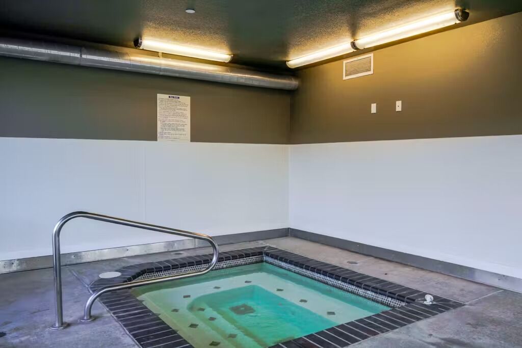 Ein kleines, rechteckiges Whirlpool-Becken mit Metallleiter, umgeben von einem gefliesten Boden und Wänden in zweifarbiger Gestaltung.
