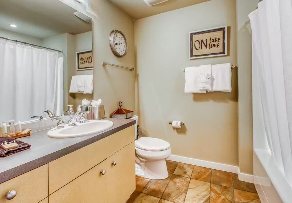 A bathroom with a sink, mirror, clock, and a towel rack.