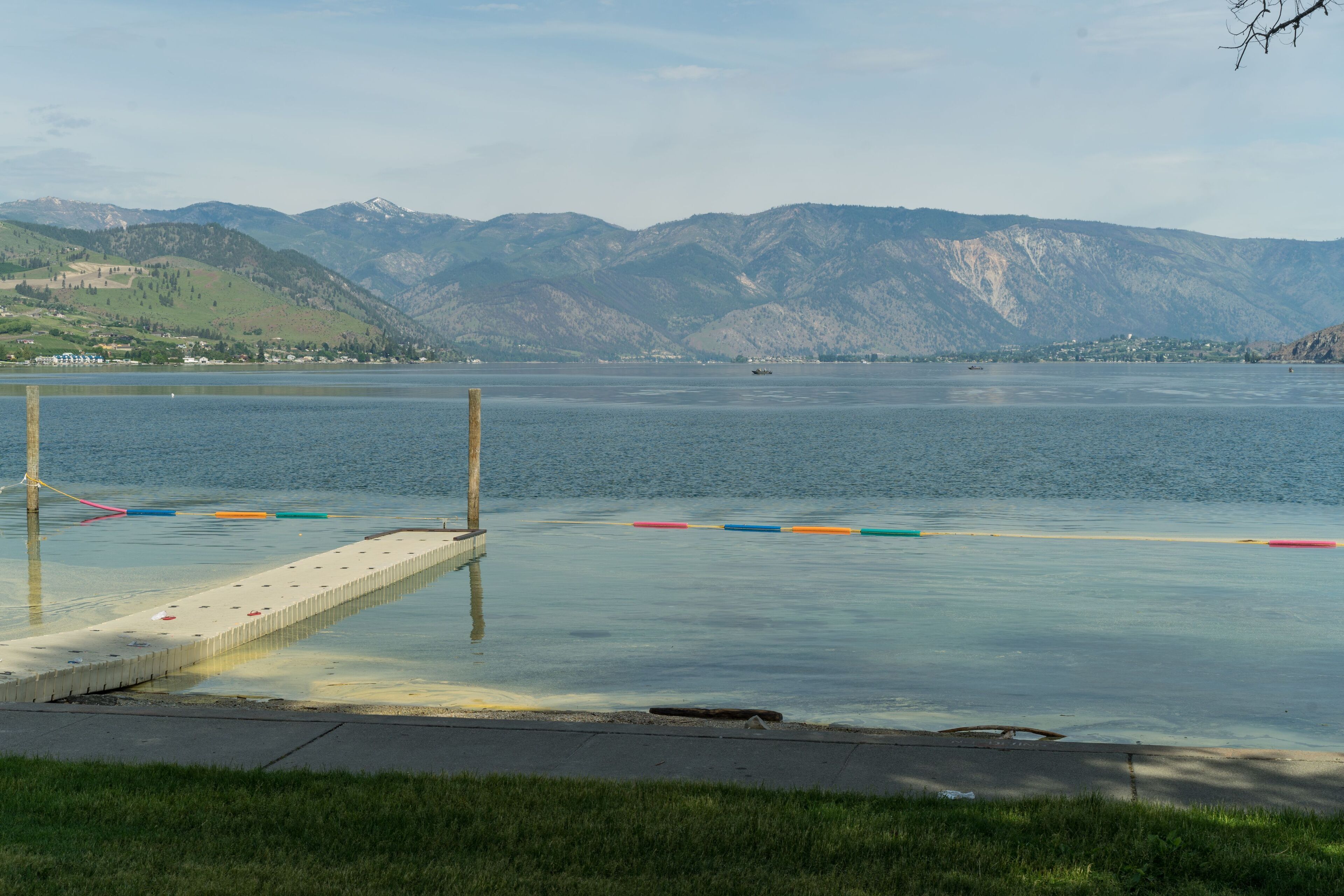 Blick auf einen See mit Bergen im Hintergrund, eine Anlegestelle und bunte Bojen.
