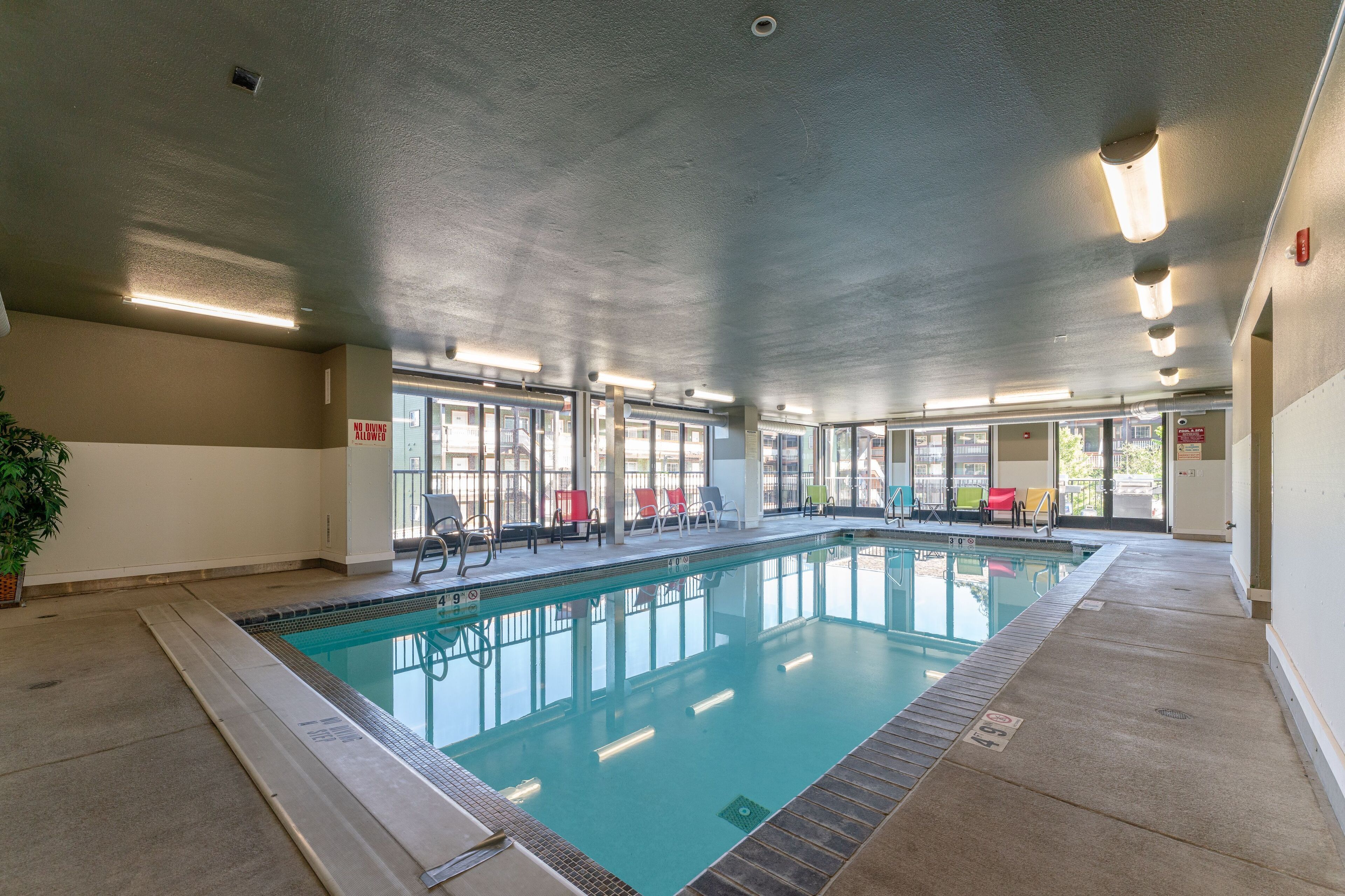 An indoor swimming pool with clear glass walls, a tiled floor, and a ceiling with recessed lighting.