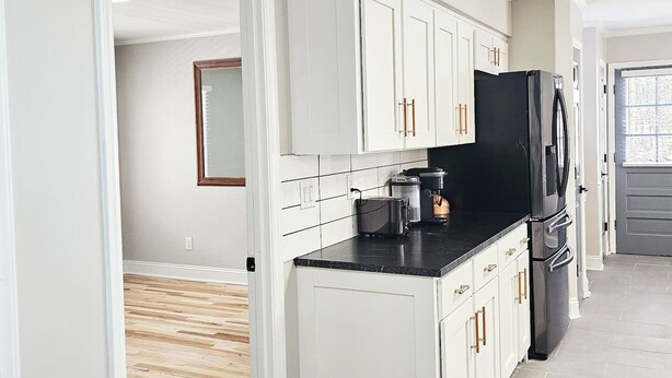 A modern kitchen with white cabinets, a black refrigerator, and a coffee maker on the counter. - 3 Bedroom House at Pine Forest Hideaway Near UNC (Chapel Hill)