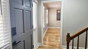 A hallway with a wooden floor, a gray door, and white-framed windows. - 3 Bedroom House at Pine Forest Hideaway Near UNC (Chapel Hill)