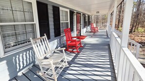 A porch with white railings, a rocking chair, and a red chair. - 3 Bedroom House at Pine Forest Hideaway Near UNC (Chapel Hill)