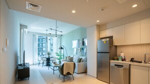 Uma cozinha moderna com eletrodomésticos de aço inoxidável, sala de jantar com mesa e cadeiras, e sala de estar com sofá e televisão.