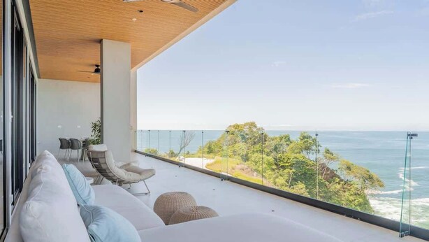 A balcony with a view of the ocean, a sofa, and a chair.