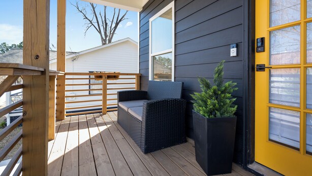 A wooden deck with a wicker sofa and a potted plant, a yellow door, and a window with a view of a house and bare tree. - 4BR/3BA Home Near Downtown ATL, Stadium & Beltline (Atlanta)