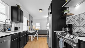 A modern kitchen with black cabinets, a stainless steel refrigerator, and a built-in oven. - 4BR/3BA Home Near Downtown ATL, Stadium & Beltline (Atlanta)