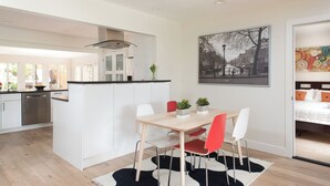 A modern kitchen with white cabinets, a central island, and a dining area with a table and chairs. - La Jolla Kid Friendly Beach House (San Diego)