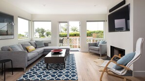 A modern living room with a grey sectional sofa, a coffee table, a patterned rug, a white armchair, and a fireplace. - La Jolla Kid Friendly Beach House (San Diego)