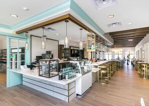 A modern cafe with a central counter, bar stools, and a kitchen area visible in the background.
