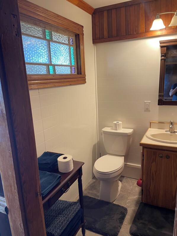 A bathroom with a toilet, sink, and a window with stained glass. - The Foreman's Cabin on amazing location (Hepburn)