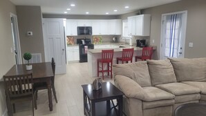 A modern kitchen with white cabinets, a central island with red chairs, and a dining area with a wooden table and chairs.
