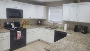 A kitchen with white cabinets, a black stove, a microwave, a sink, and a coffee maker.