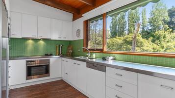 A modern kitchen with white cabinets, a green tiled backsplash, a stainless steel oven, and a window with a view of trees.