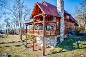 A log cabin with a stone chimney, wooden balcony, and multiple windows. - Grin'Inn Bear It at Eagles Nest - Village home with views, 2 king beds (Banner Elk)