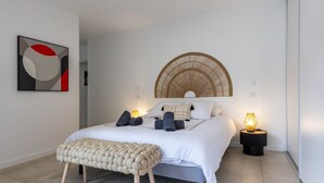 Ein modernes Schlafzimmer mit Bett, Nachttischlampen, einem Wandbild und einem gewebten Kopfteil.