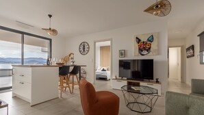 Ein modernes Wohnzimmer mit großem Fernseher, einem Essbereich und einer Küche.